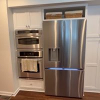 Stainless steel French door refrigerator next to built-in double wall ovens and white cabinets