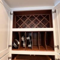 Vertical bakeware storage slots and upper wine rack built into a tall white cabinet