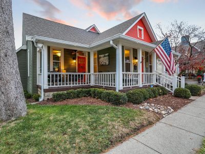 Zionsville Home Exterior Renovation with Wraparound Porch Renovated green home exterior with a wraparound porch, red accents, and updated landscaping at dusk